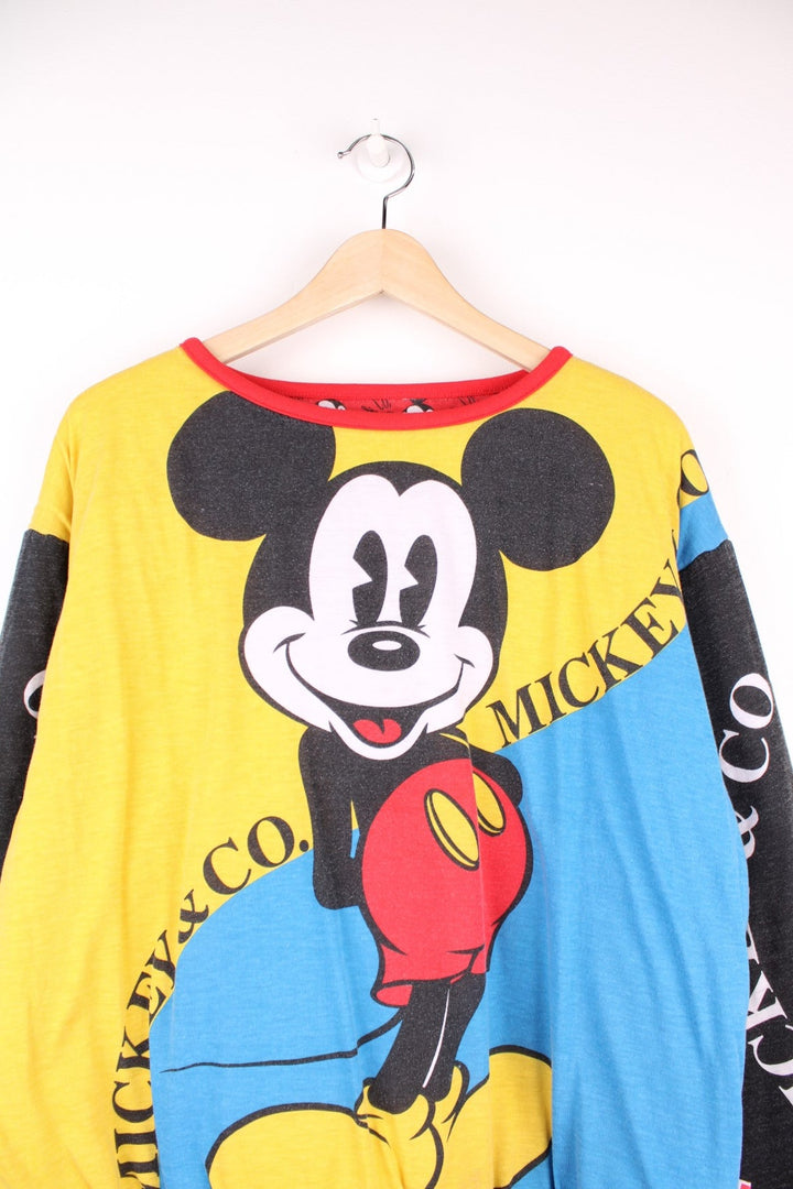 80s/90s Disney reversible lined sweatshirt with one red, yellow, and blue colourblocking side featuring a large Mickey Mouse graphic and text reading 'Mickey and Co.', and one red side with a repeating Mickey head pattern. 