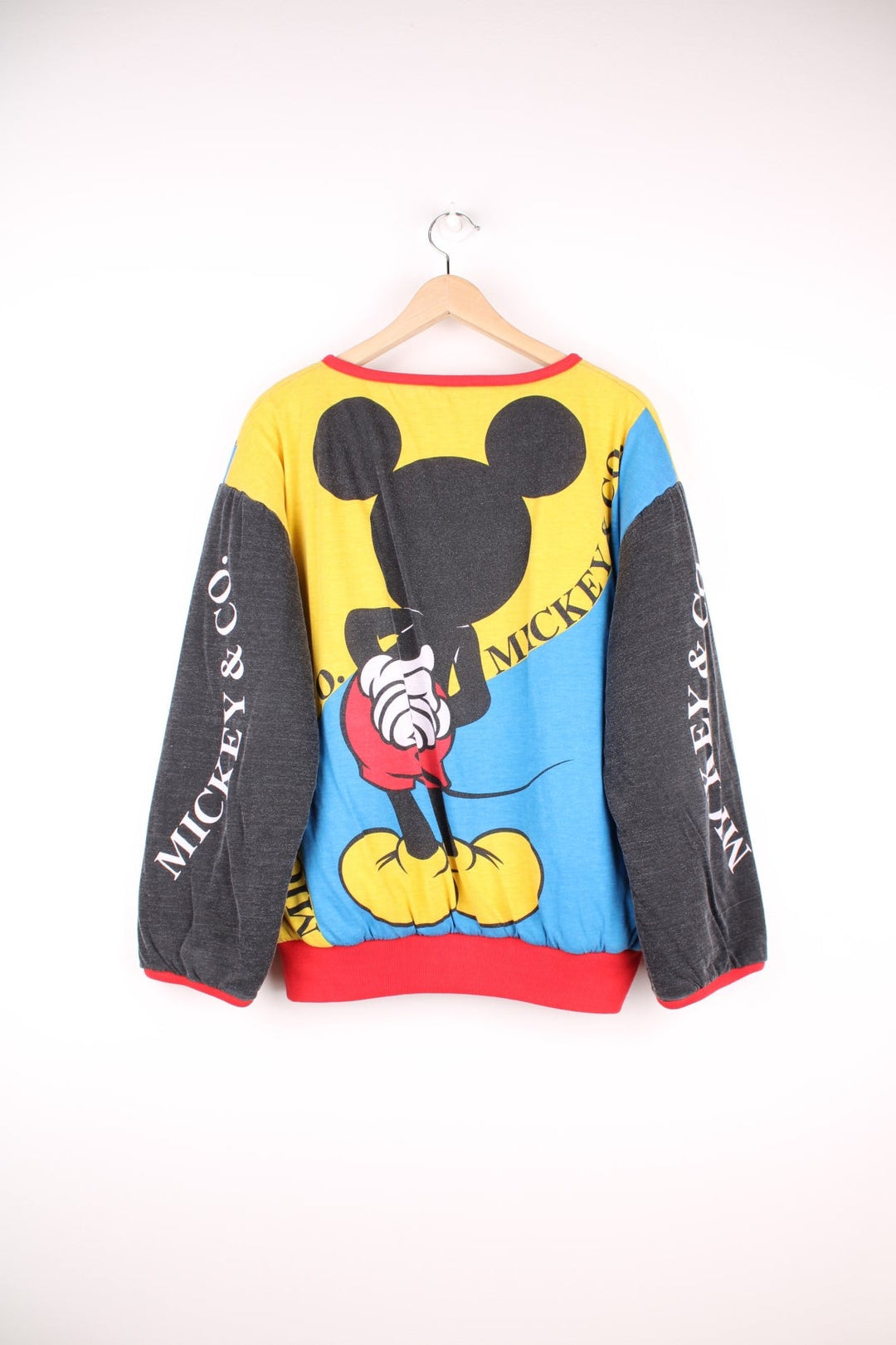 80s/90s Disney reversible lined sweatshirt with one red, yellow, and blue colourblocking side featuring a large Mickey Mouse graphic and text reading 'Mickey and Co.', and one red side with a repeating Mickey head pattern. 