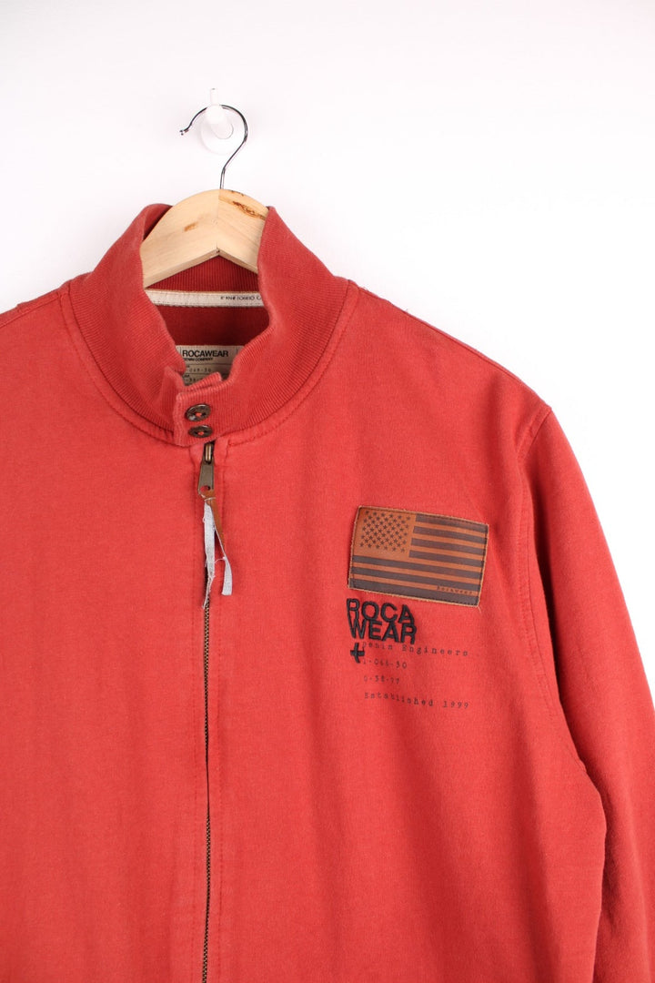  Y2K Rocawear Zip-through Sweatshirt in a red colourway with embroidered logo, button-close pockets and multiple patches stitched to the front and right sleeve.