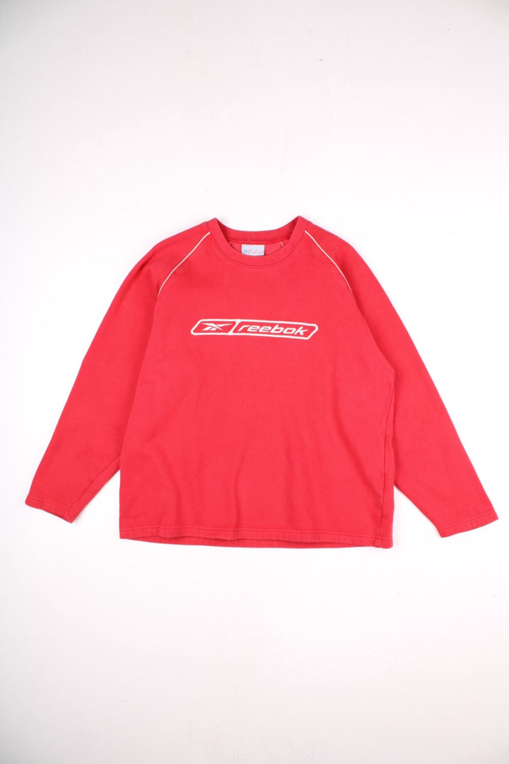 Vintage Reebok Sweatshirt in a red colourway with a large Reebok logo embroidered on the front, and white piping detail around the shoulder seams. 