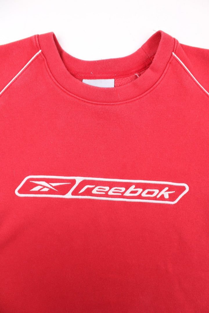 Vintage Reebok Sweatshirt in a red colourway with a large Reebok logo embroidered on the front, and white piping detail around the shoulder seams. 