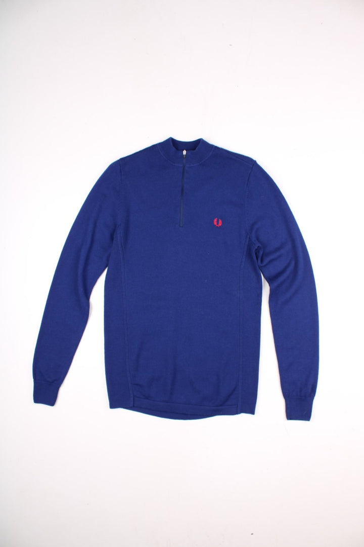 Fred Perry X Bradley Wiggins merino knit jumper in a blue colourway. The Fred Perry logo is embroidered on the front. The knit has side panels, and a small zipped back pocket similar to a cycling jersey. Slim fit silhouette. 