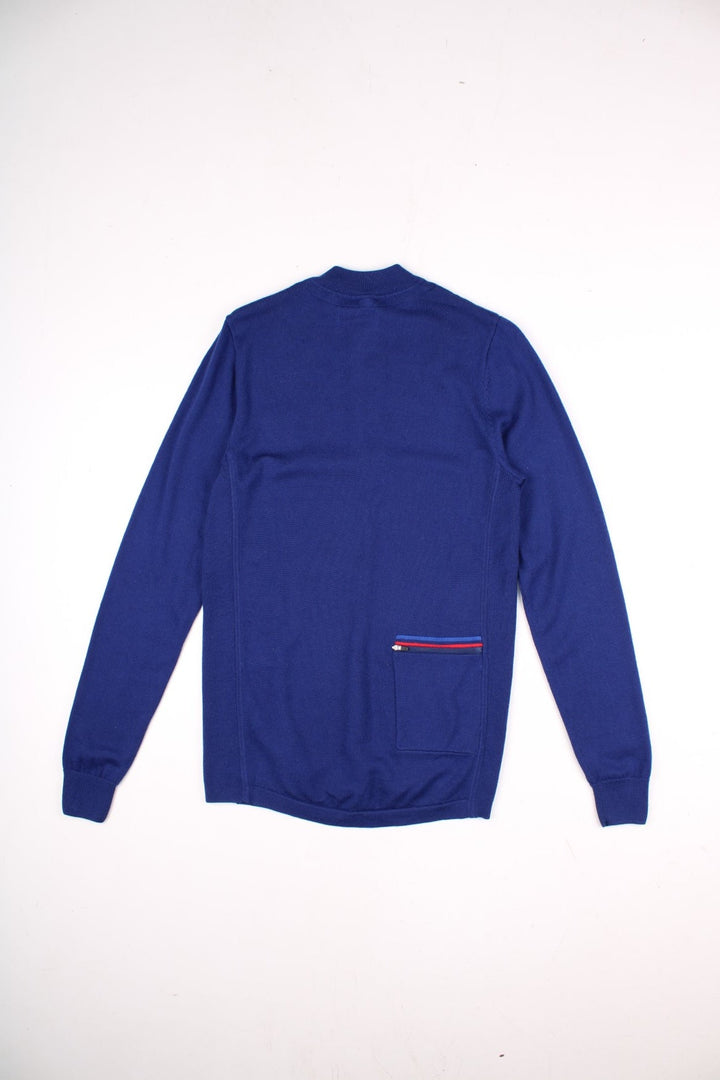 Fred Perry X Bradley Wiggins merino knit jumper in a blue colourway. The Fred Perry logo is embroidered on the front. The knit has side panels, and a small zipped back pocket similar to a cycling jersey. Slim fit silhouette. 