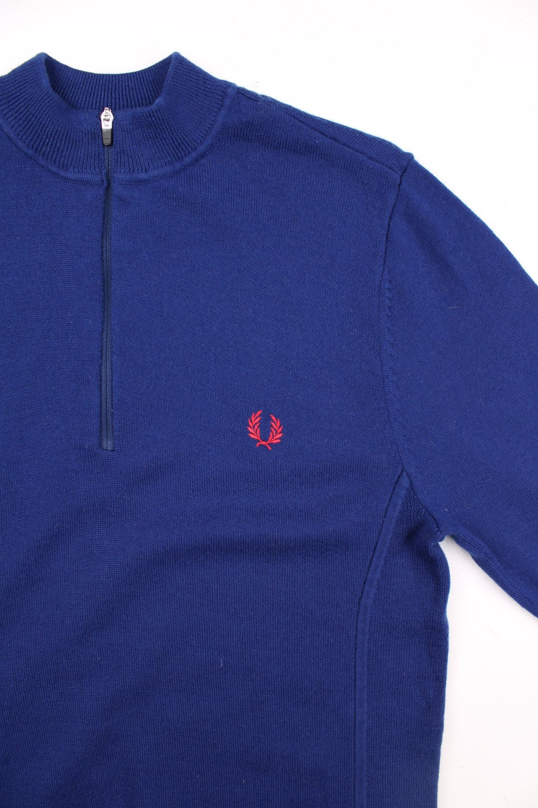 Fred Perry X Bradley Wiggins merino knit jumper in a blue colourway. The Fred Perry logo is embroidered on the front. The knit has side panels, and a small zipped back pocket similar to a cycling jersey. Slim fit silhouette. 