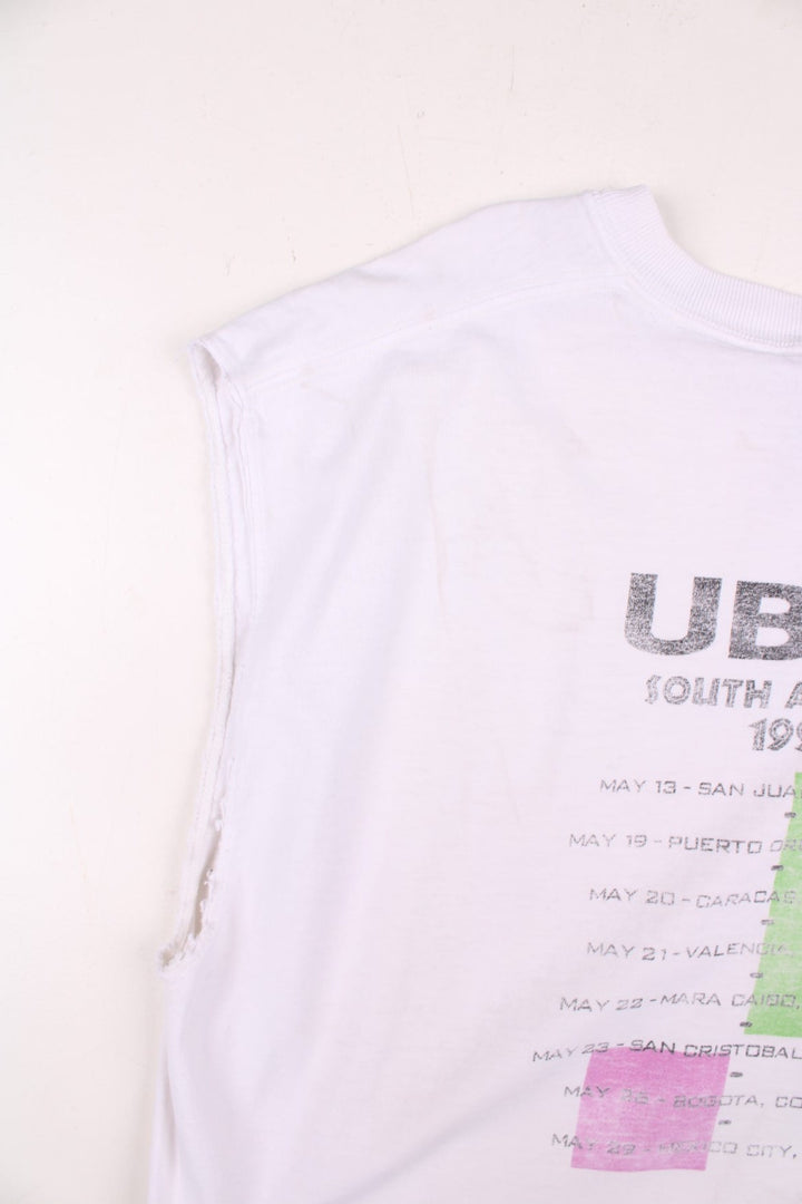 Vintage 1999 UB40 South America Tour Vest in a white colourway with the logo and art graphic printed on the front but is heavily faded, and on the back are the tour dates printed, this garment was a t-shirt which has had its sleeves removed.