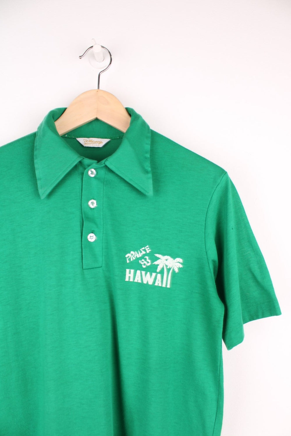 Vintage dagger collared tee in green with 'Praise '83 Hawaii' spellout and palm tree design on the upper right, with two buttons. 