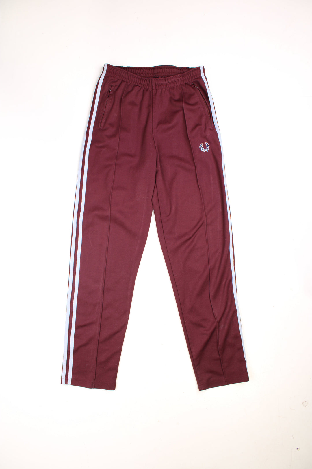 Fred Perry Tracksuit Bottoms in a burgundy red colourway with light blue stripes going down the sides, has an elasticated waist with drawstring, zip up side pockets, and the logo embroidered on the front. 