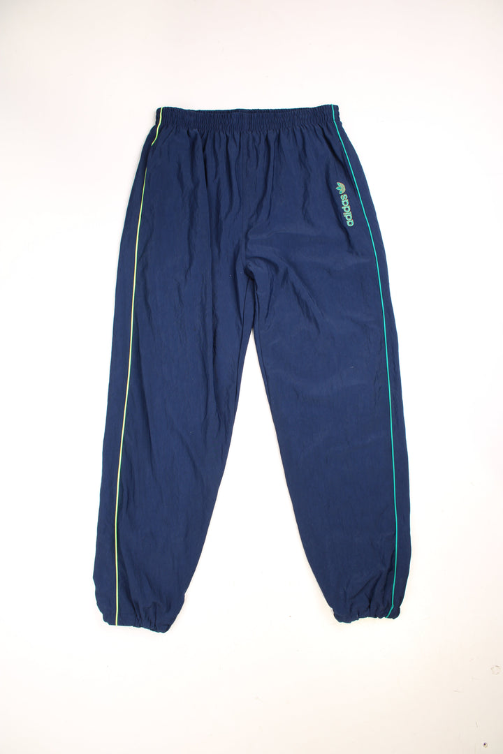 Adidas Tracksuit Bottoms in a blue colourway with a green stripe going down the sides, has an elasticated waist with drawstring, pockets, cotton lining, and the spell out logo embroidered on the front. 