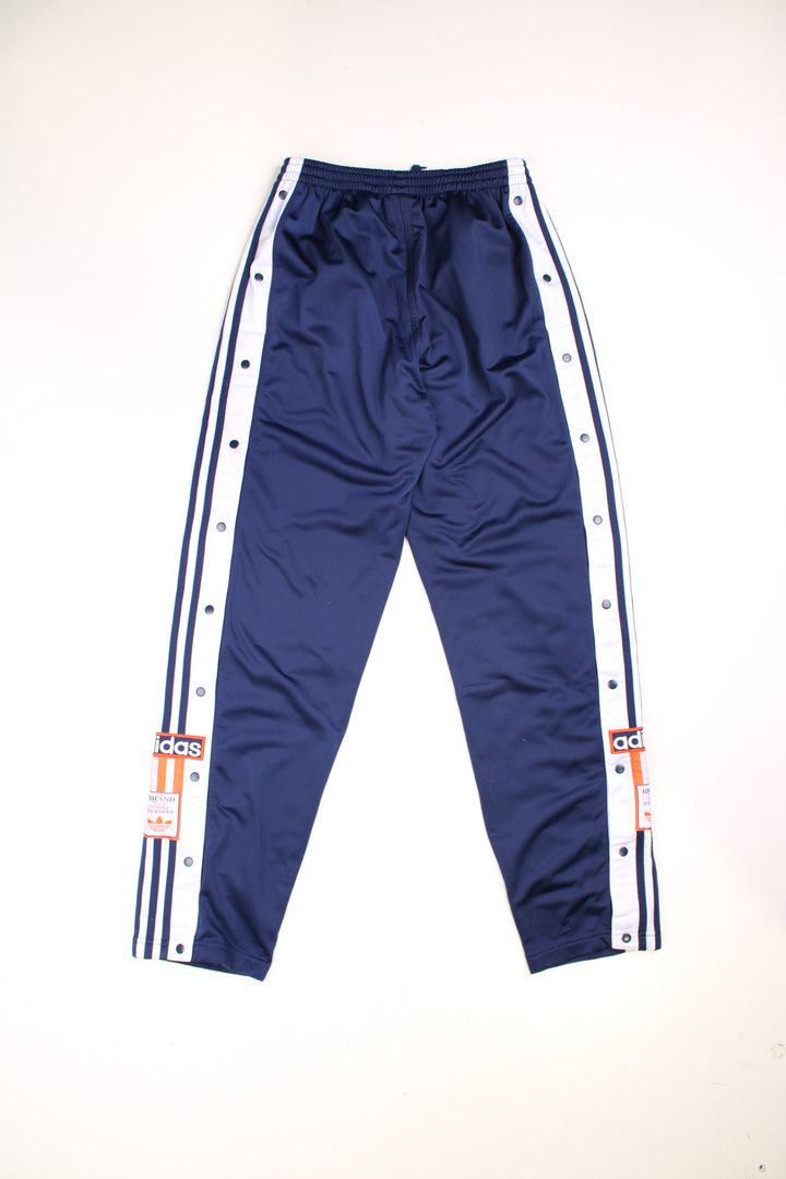 Vintage  Popper Tracksuit Bottoms in a  colourway with stripes going down the sides, has an elasticated waist with drawstring, zip up side pockets, and the logo embroidered on the down the legs. 