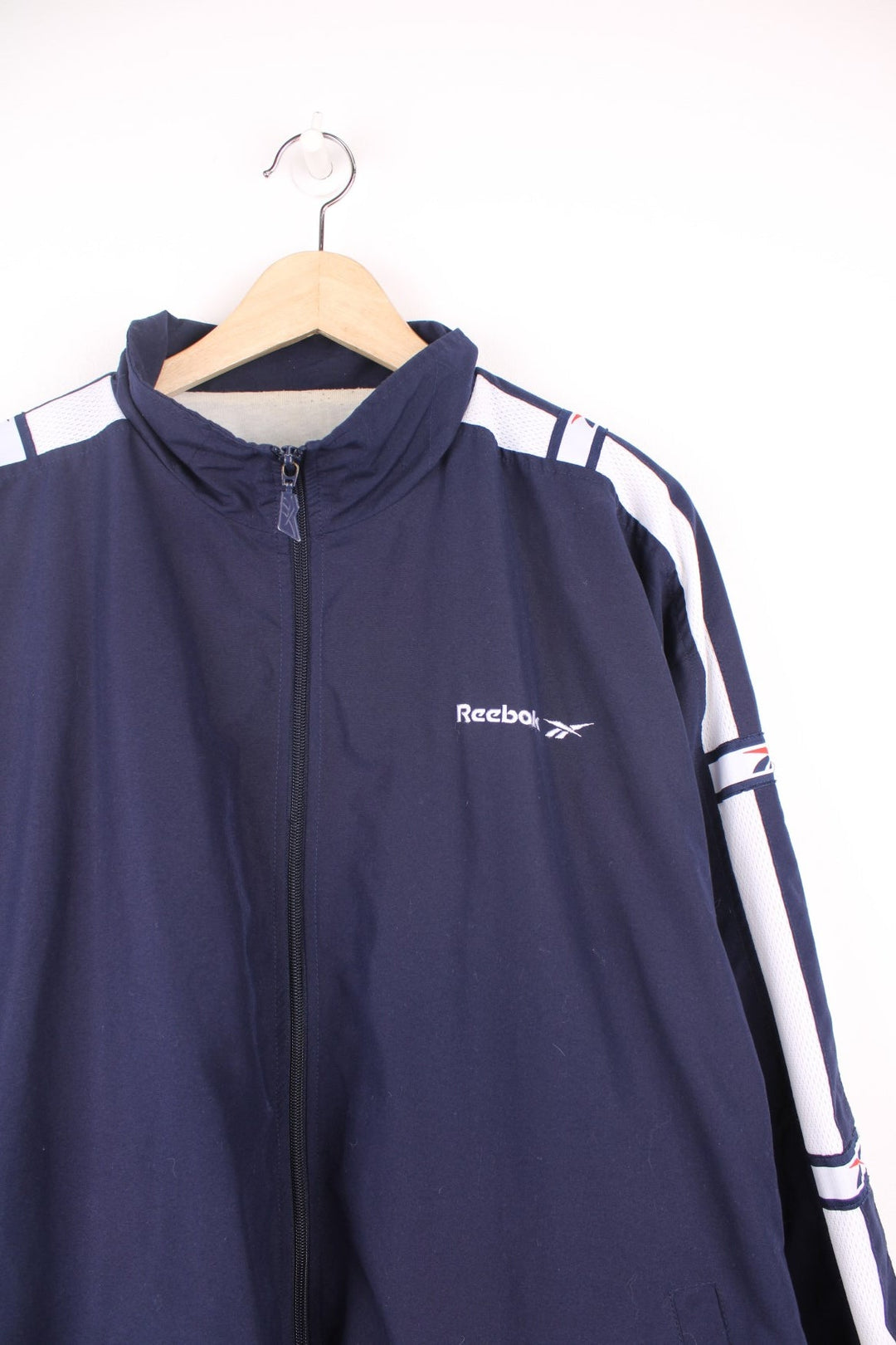 Vintage Reebok tracksuit top in navy blue. Features embroidered logo on the chest, and white tape sleeve with repeated logo.