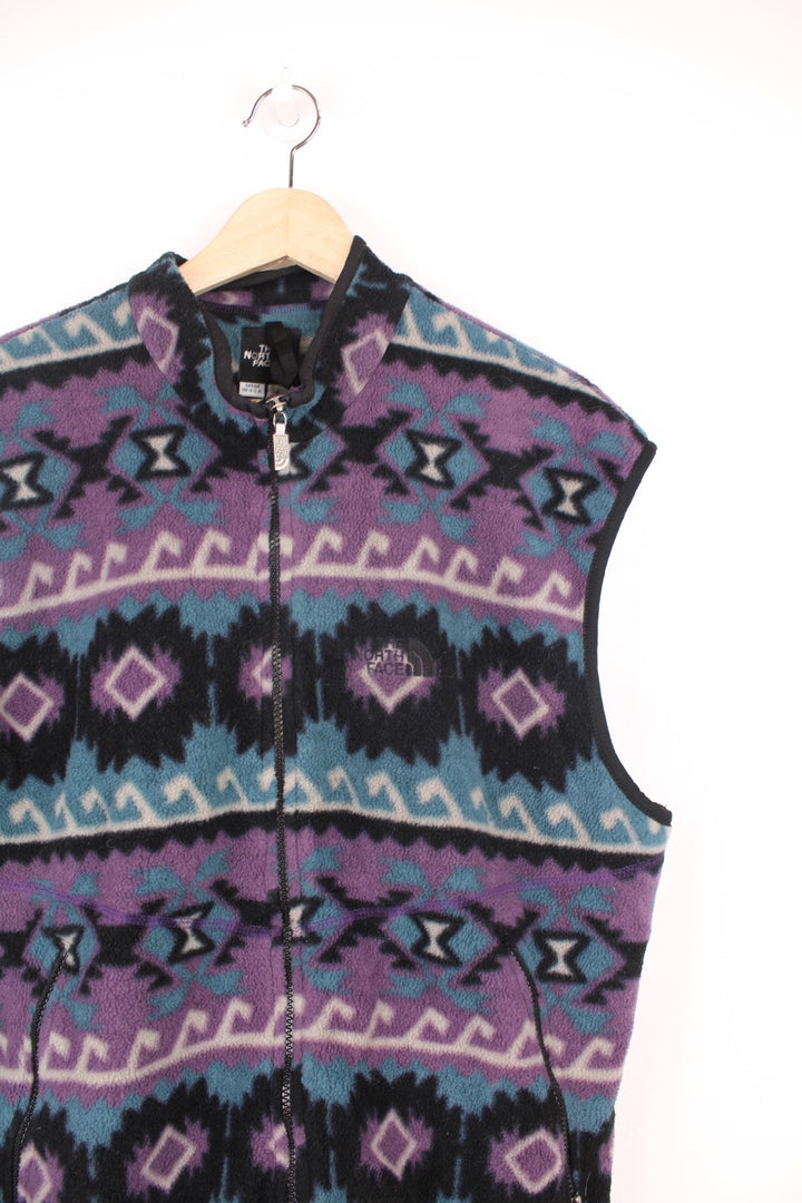 The North Face zip through fleece gilet in purple, blue and black aztec pattern. Features embroidered logo on the chest.