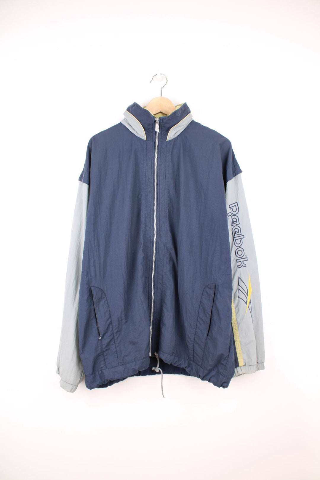 Vintage Reebok zip through tracksuit top in grey and blue. Features embroidered spell out logo down the sleeve, logo on the back, and a pack away hood.  