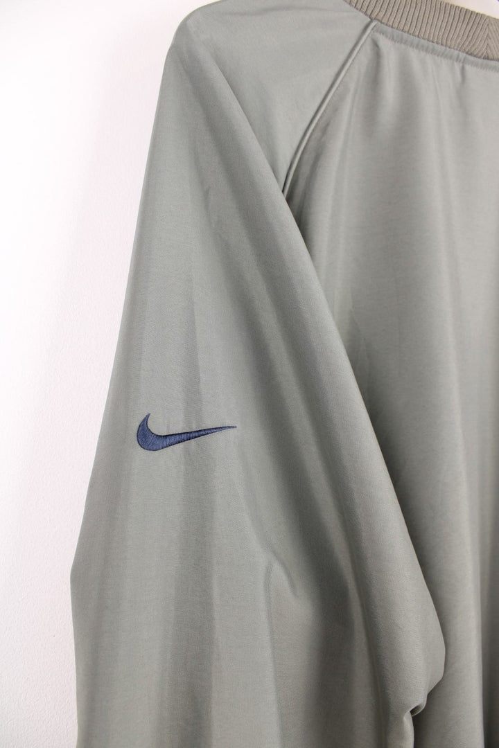 Nike golf pullover in khaki with two zipped pockets and a black embroidered swoosh on one sleeve.