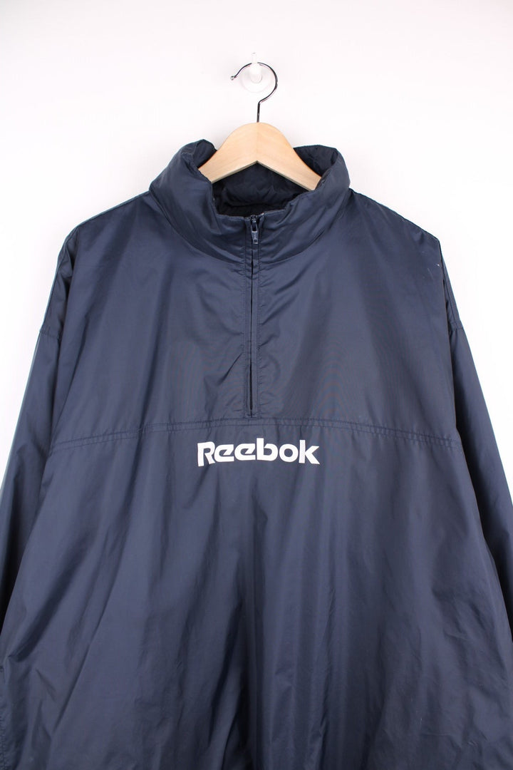 Reebok 1/2 zip shell jacket in navy blue with two pockets and drawstring waist adjustment. 