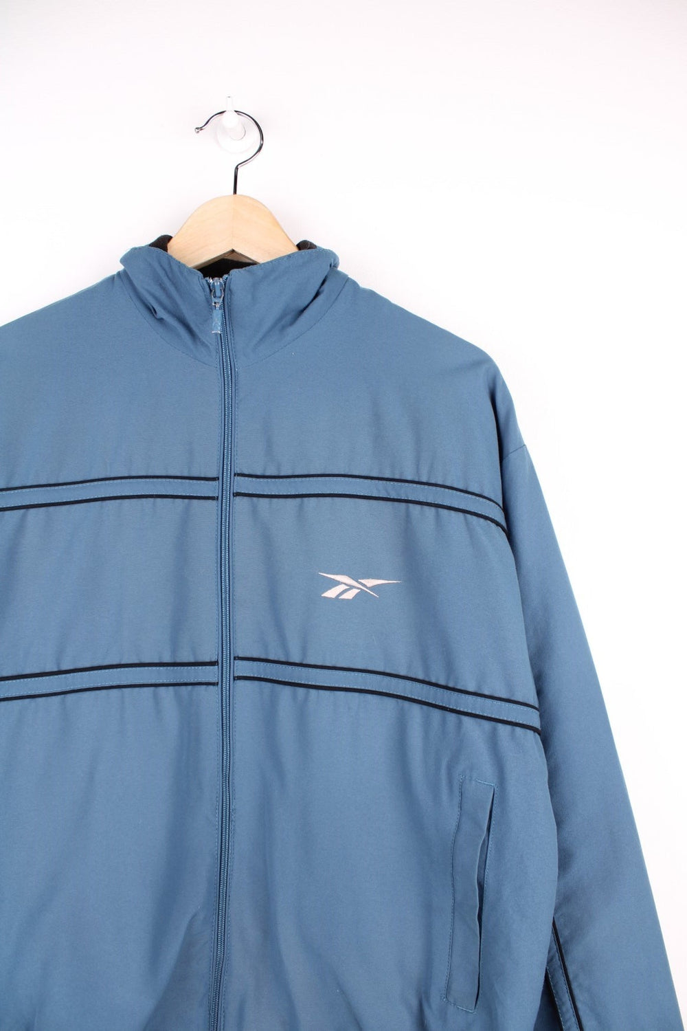 Reebok zip through track jacket in blue with black piping, two pockets, and embroidered logos in white on the front and back. 