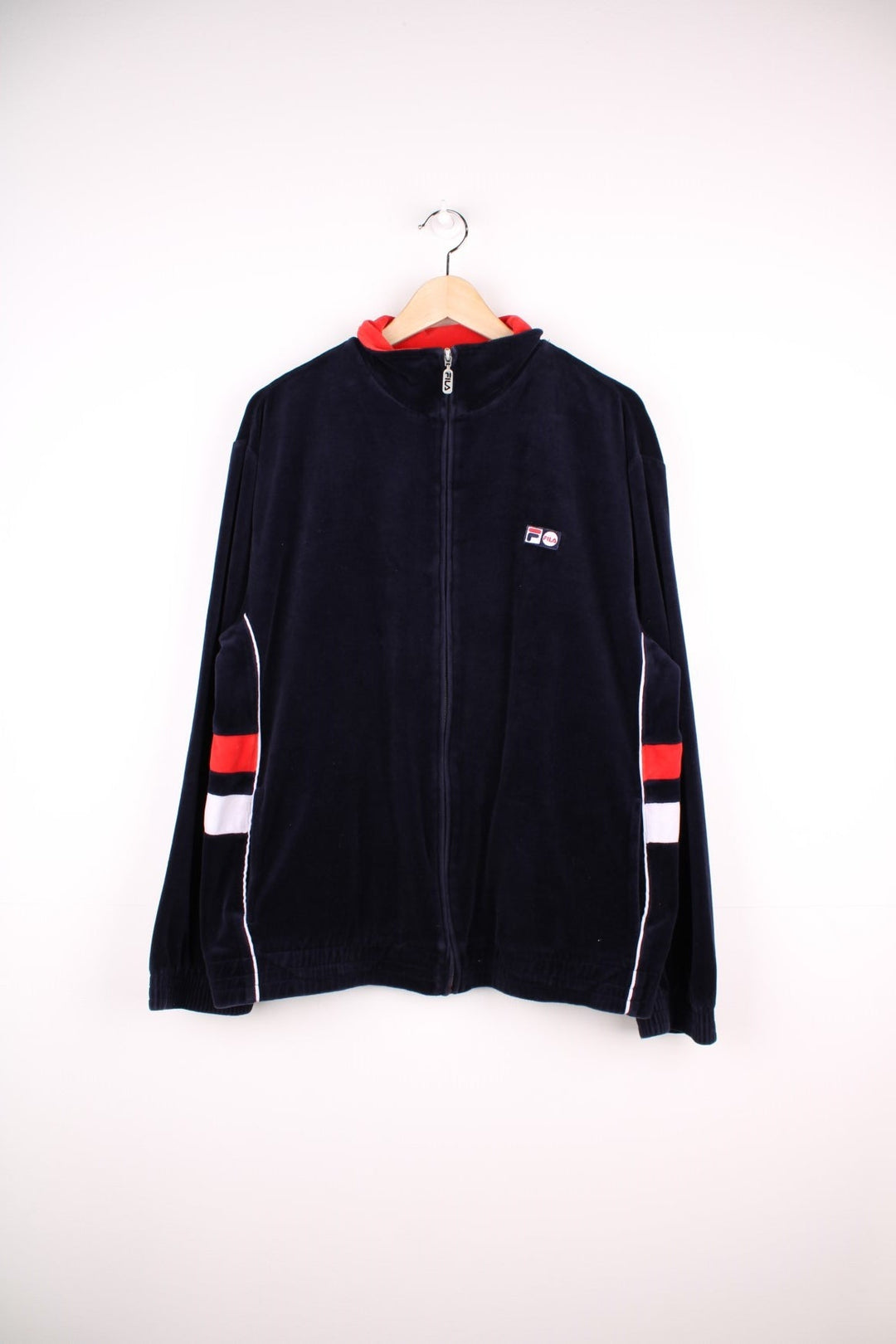 Fila zip-through tracksuit top in navy blue velour with red and white accent stripes on the sleeves, two pockets and an embroidered logo patch on the chest. 