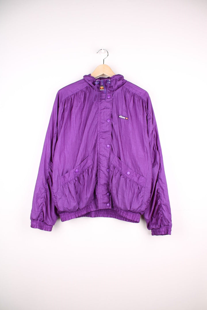 Ellesse track top/shell jacket in bright purple with two pockets, an embroidered logo, snap closure, and toggle adjusters on the collar. 