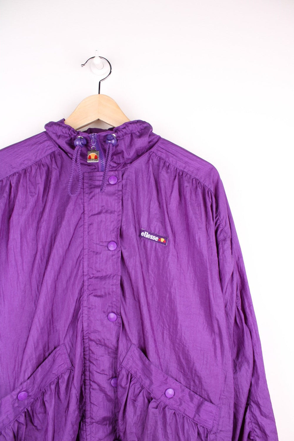 Ellesse track top/shell jacket in bright purple with two pockets, an embroidered logo, snap closure, and toggle adjusters on the collar. 