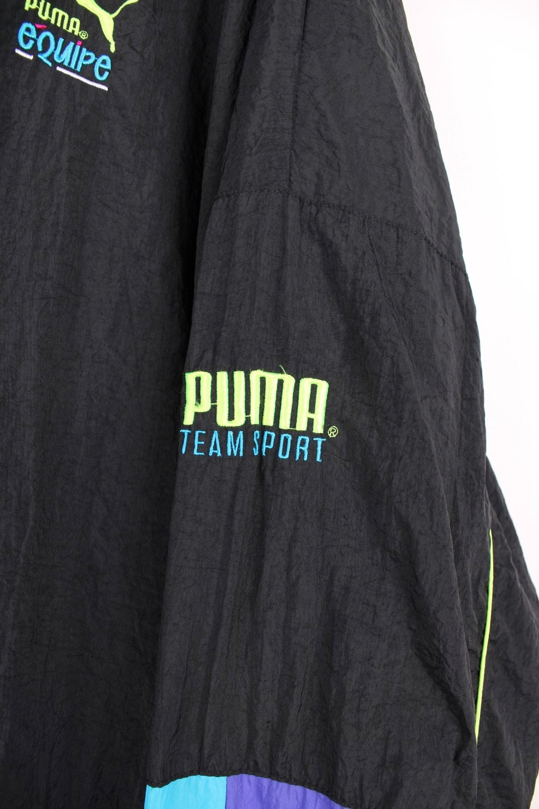 90s Puma Equipe track top/shell jacket in black with blue, green and purple accents, two pockets, zip closure and an embroidered logo.