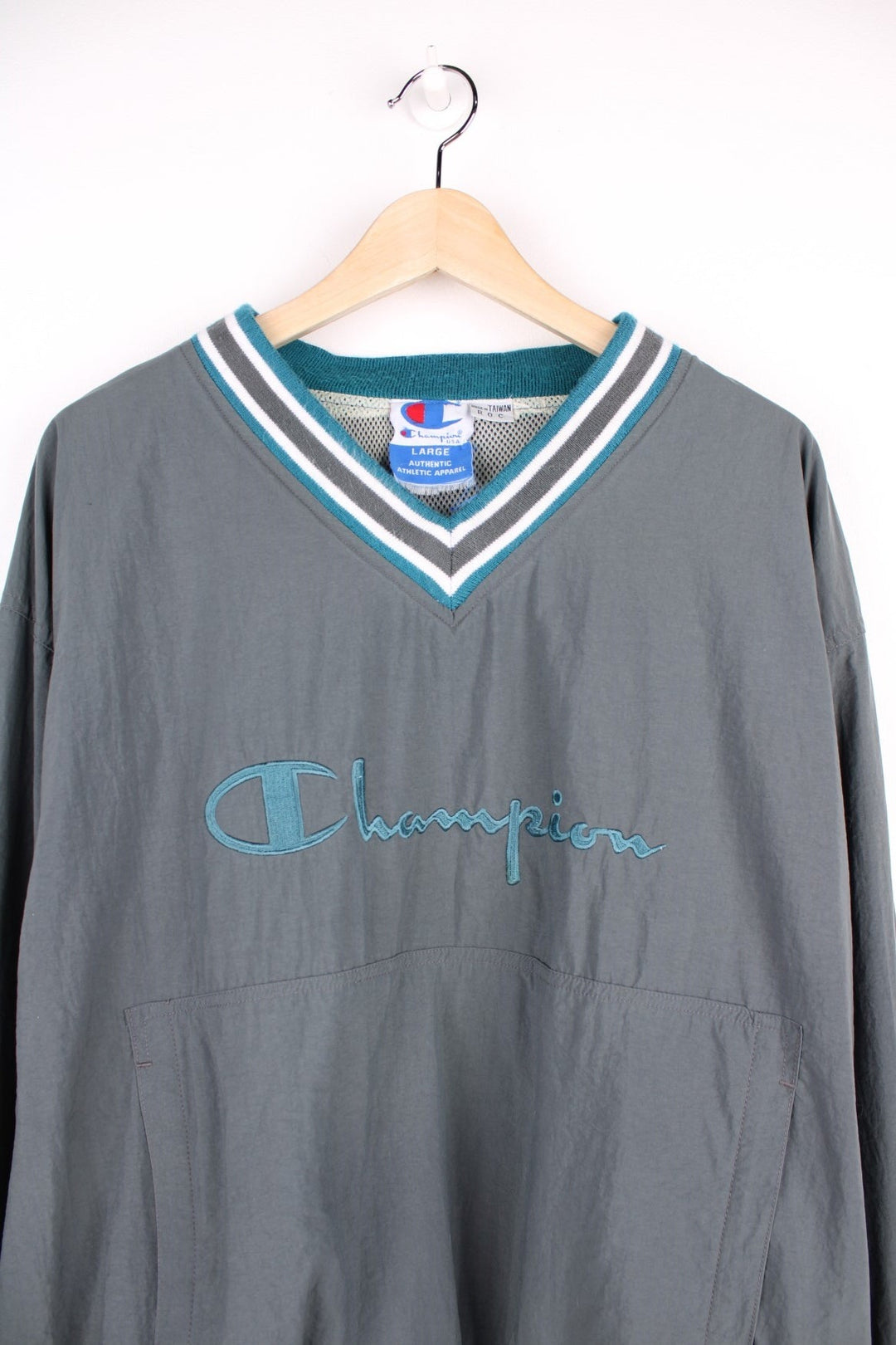 Champion v-neck pullover track top in grey with blue and white striped detailing on hem, cuffs and collar, and embroidered logos on the chest, sleeve and back. 