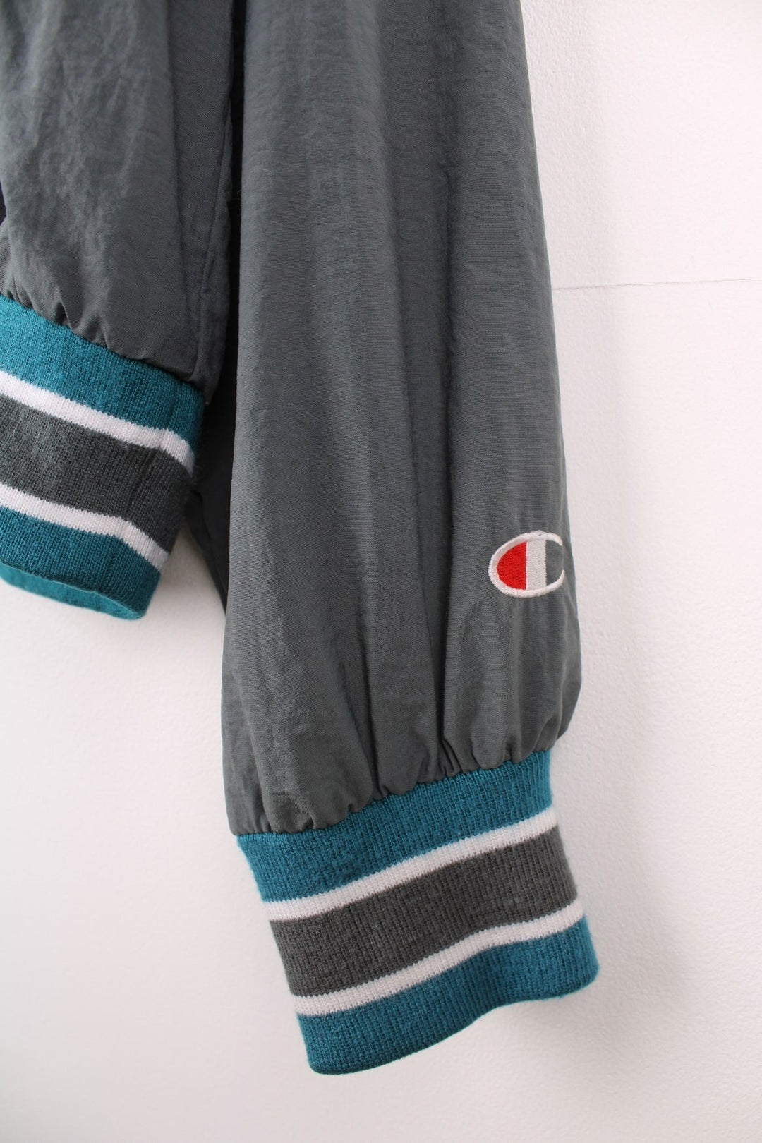 Champion v-neck pullover track top in grey with blue and white striped detailing on hem, cuffs and collar, and embroidered logos on the chest, sleeve and back. 