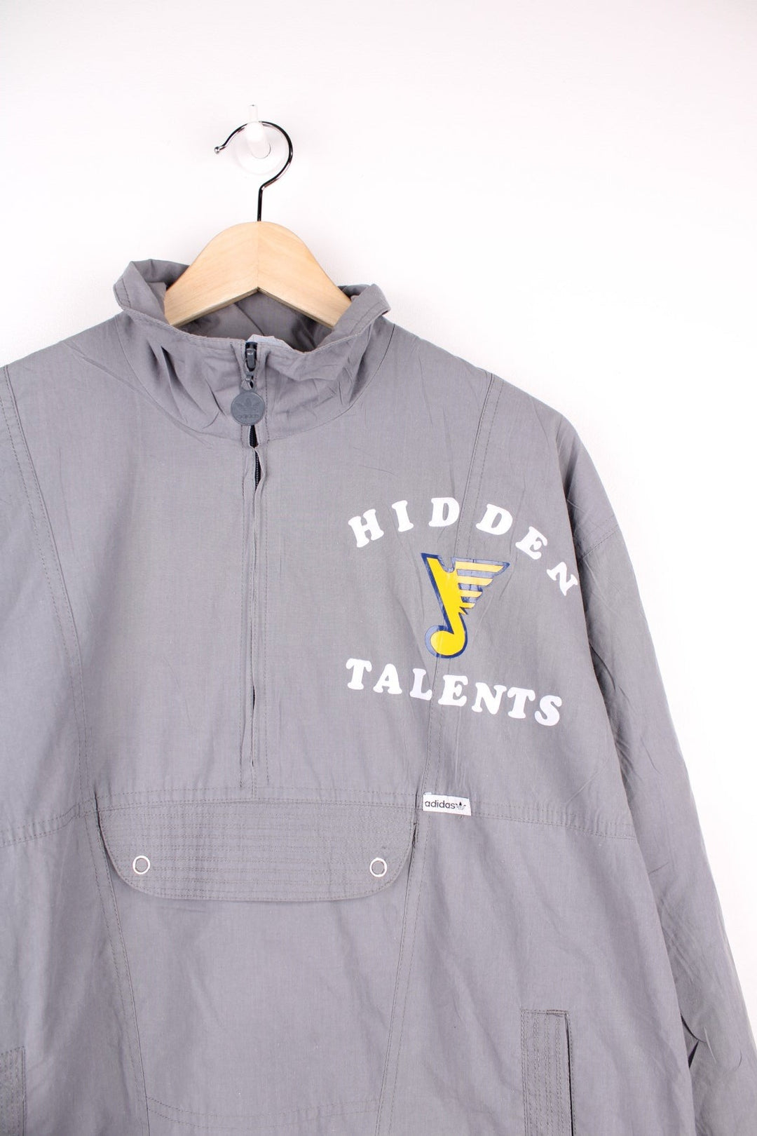 Adidas 1/2 zip pullover track top in grey with three pockets and printed text reading 'Hidden Talents' and a musical note emblem. 