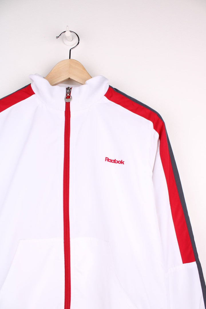 Reebok Classic zip-through tracksuit top in white with red and grey stripes on the sleeves, two pockets and embroidered logos on the chest and back.  