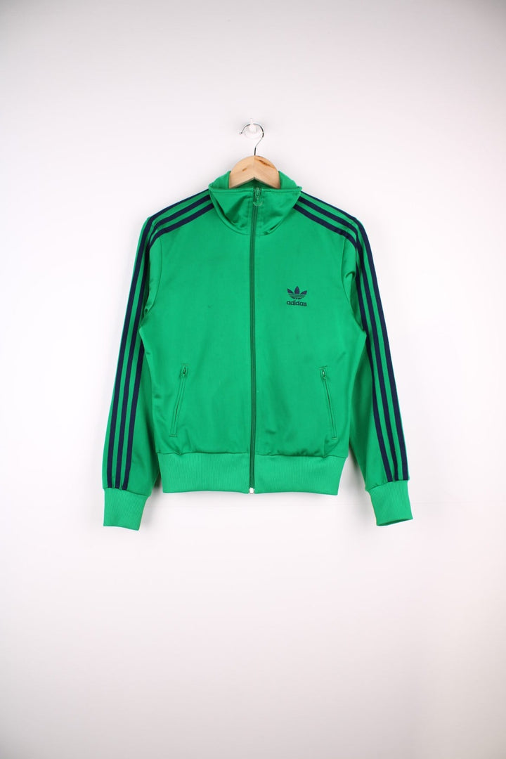 Adidas Tracksuit Top in a green colourway with the iconic three stripes going down the sleeves in navy blue, zip up closure and has side pockets and the logo embroidered on the front and larger on the back.