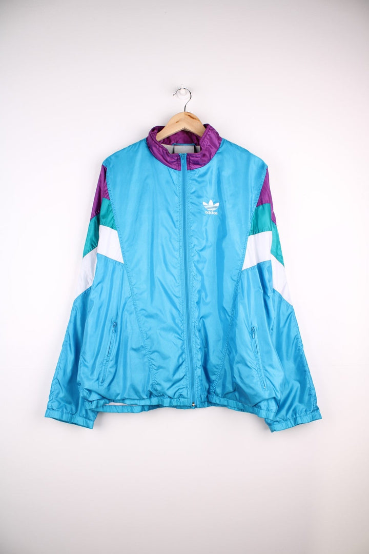 Vintage Adidas Tracksuit Jacket in a blue, purple and white patterned colourway, zip up closure and has side pockets, cotton lining, and the logo embroidered on the front.