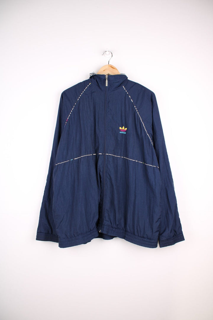 Adidas Tracksuit Jacket in a navy blue colourway with patterned stripes going around the sides, zip up closure and has side pockets, cotton lining, and the logo embroidered on the front.