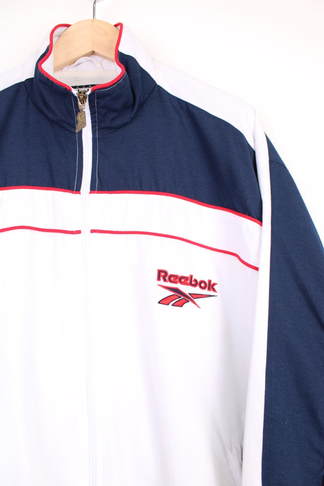 Reebok all white zip through tracksuit top, features embroidered logo on the chest and cuff ,navy blue panels and red piping. 