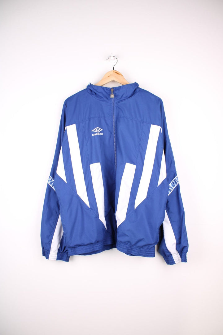 Vintage Umbro Tracksuit Jacket in a blue and white patterned colourway, zip up closure and has side pockets, and the logo embroidered on the front and back.