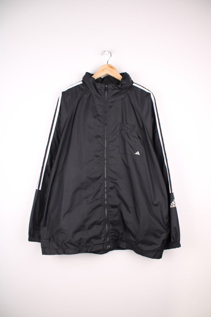 Adidas Windbreaker in a black colourway with the iconic three stripes going down the sleeves, zip up closure, has multiple pockets, hidden hood, and the logo embroidered on the front and larger on the back.