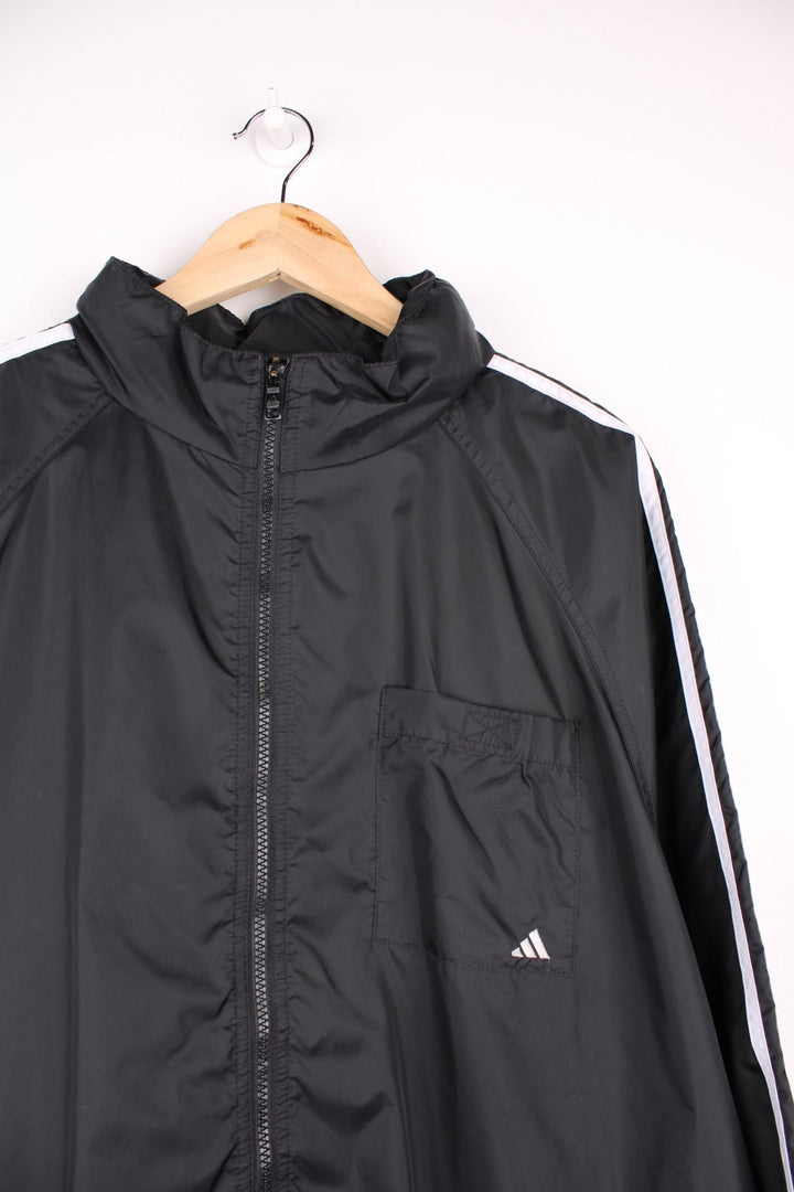  Windbreaker in a  colourway with the iconic three stripes going down the sleeves, zip up closure, has multiple pockets, hidden hood, and the logo embroidered on the front and larger on the back.