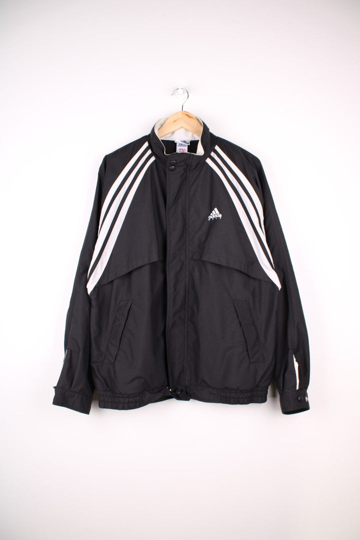 Adidas Golf Jacket in a black and white colourway with the iconic three stripes going down the sides, zip up closure, side pockets, and has the logo embroidered on the front.