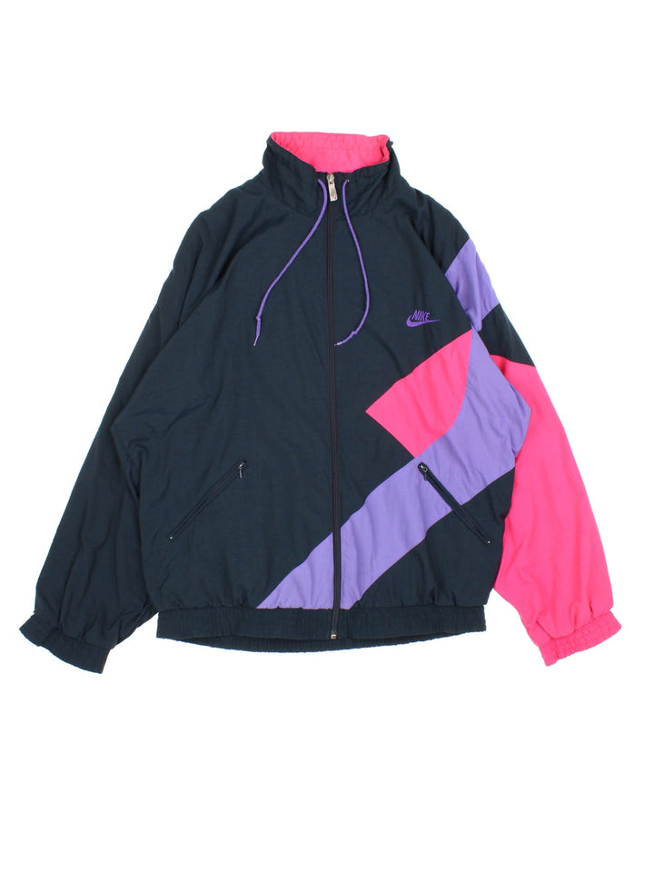 Vintage 90's Nike Windbreaker Jacket in a black, purple and pink patterened colourway. Zips up and has side pockets, and the logo embroidered on the front.