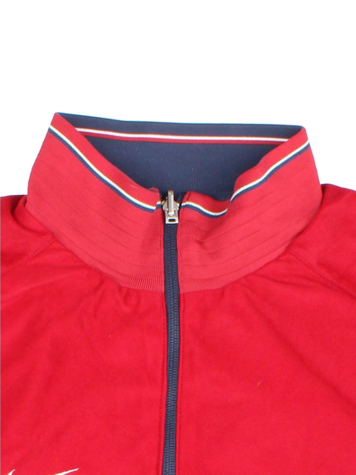 Nike 1/4 zip reversible track top in navy blue with two zipped pockets, red and white stripe detailing, and a logo on the sleeve. Reverse side is red with blue and white stripe detailing. Swoosh embroidered on the chest of both sides.