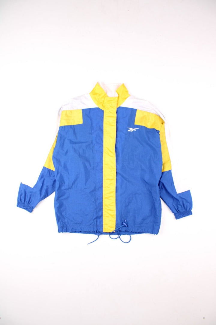 Vintage 90's Reebok Windbreaker Jacket in blue, with yellow and white panelling, two pockets, zip and velcro closure, a drawstring at the hem, and an embroidered logo on the chest and back.