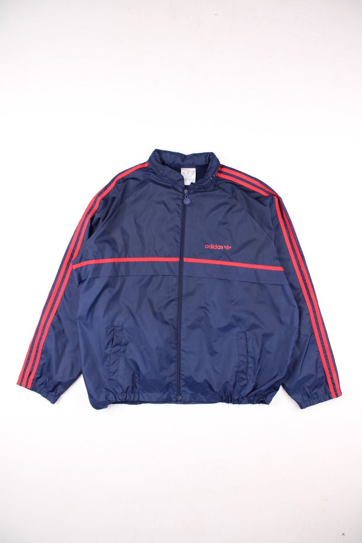 Vintage Adidas Trefoil Windbreaker Jacket in navy blue, with red three-stripe, two pockets, zip closure, a hidden hood, and the logo on the front.