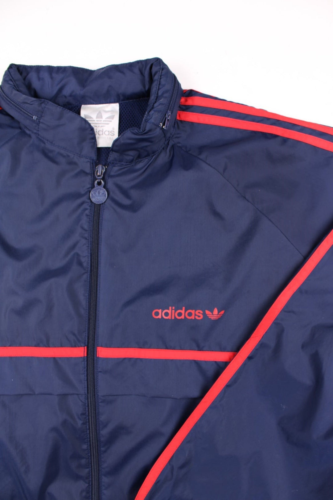 Vintage Adidas Trefoil Windbreaker Jacket in navy blue, with red three-stripe, two pockets, zip closure, a hidden hood, and the logo on the front.