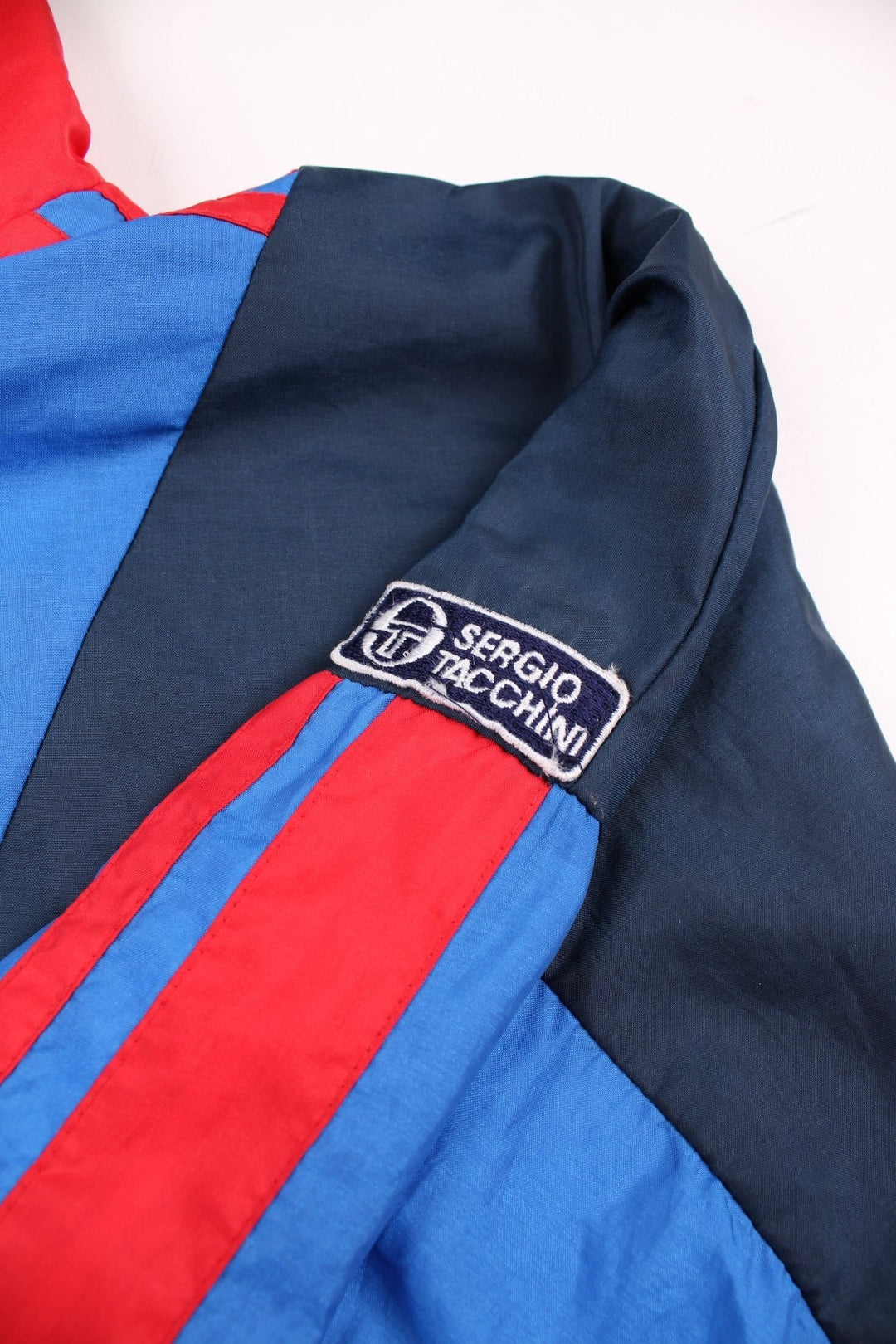 Vintage Sergio Tacchini track jacket in navy blue, with red and blue panelling, two pockets, zip closure, and an embroidered logo on the sleeve.