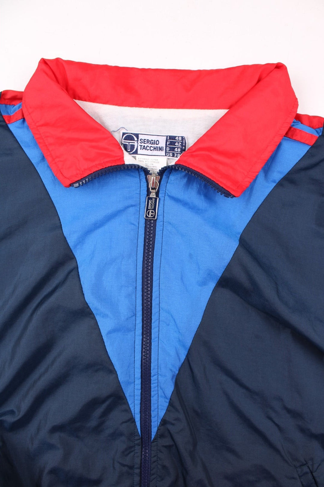 Vintage Sergio Tacchini track jacket in navy blue, with red and blue panelling, two pockets, zip closure, and an embroidered logo on the sleeve.