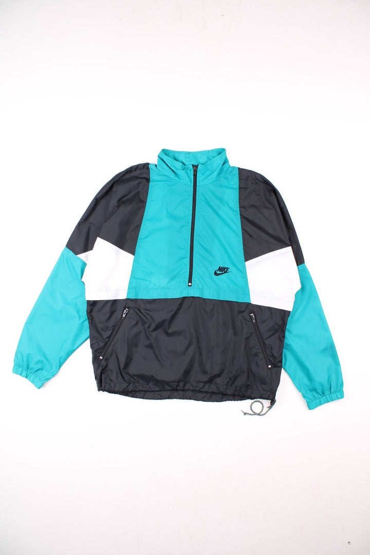 Vintage 90's Nike Pullover Windbreaker in black, with turquoise and white panelling, two pockets, half zip closure, and an embroidered logo on the chest.