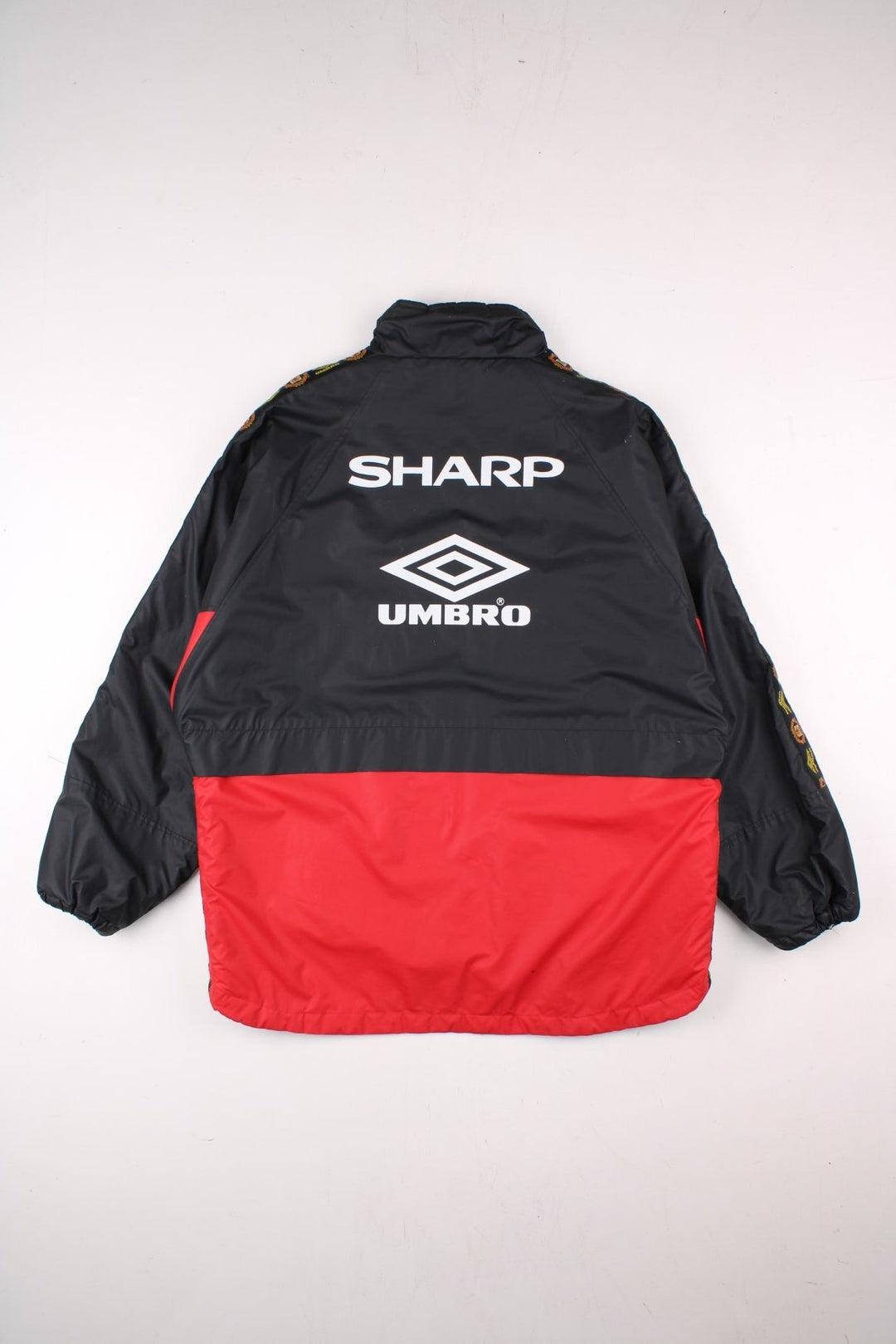 Vintage 1996/97 Manchester United Umbro Coat in black with red panelling, quilt lining, two zipped pockets, zip and snap closure, an embroidered logo on the chest and on the back big logos printed, also has logo tape down each sleeve.