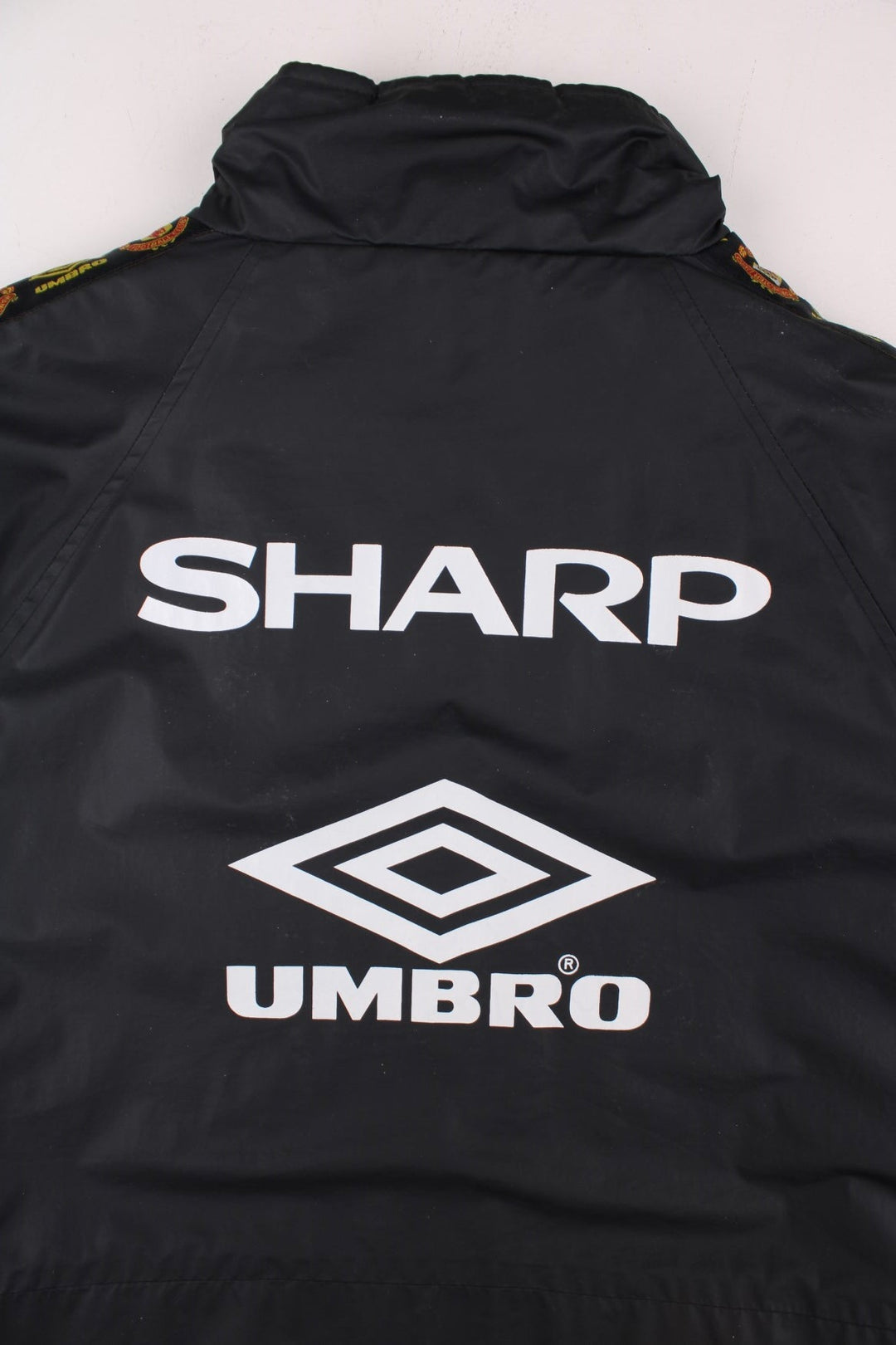 Vintage 1996/97 Manchester United Umbro Coat in black with red panelling, quilt lining, two zipped pockets, zip and snap closure, an embroidered logo on the chest and on the back big logos printed, also has logo tape down each sleeve.