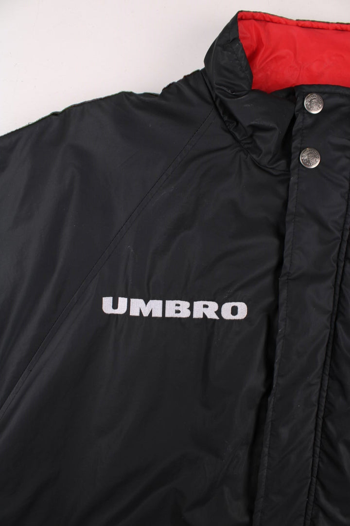 Vintage 1996/97 Manchester United Umbro Coat in black with red panelling, quilt lining, two zipped pockets, zip and snap closure, an embroidered logo on the chest and on the back big logos printed, also has logo tape down each sleeve.