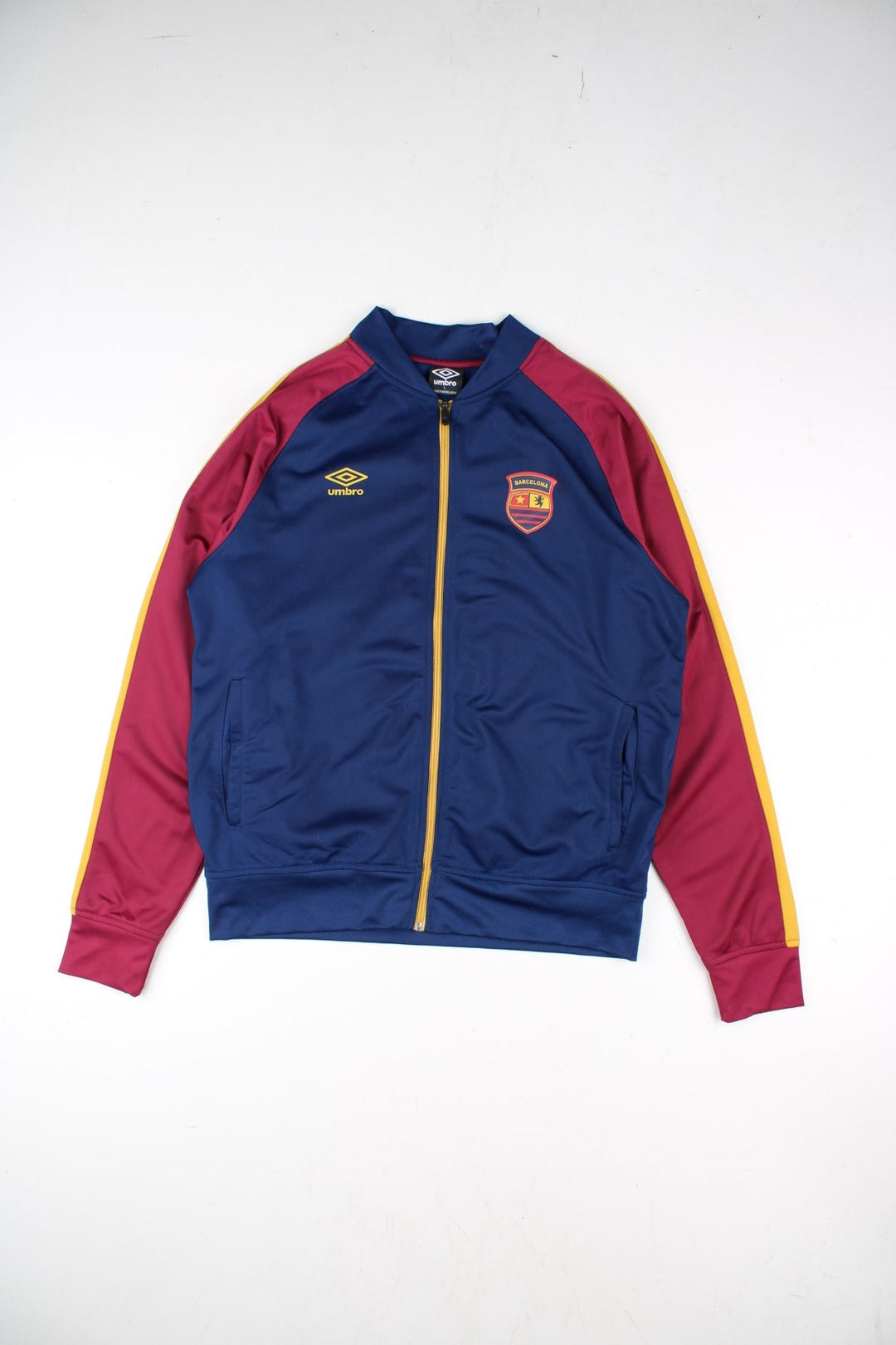 Umbro Barcelona Track Top in a blue colourway with red panelling and yellow stripe. Full zip with small club and brand logos on the front..