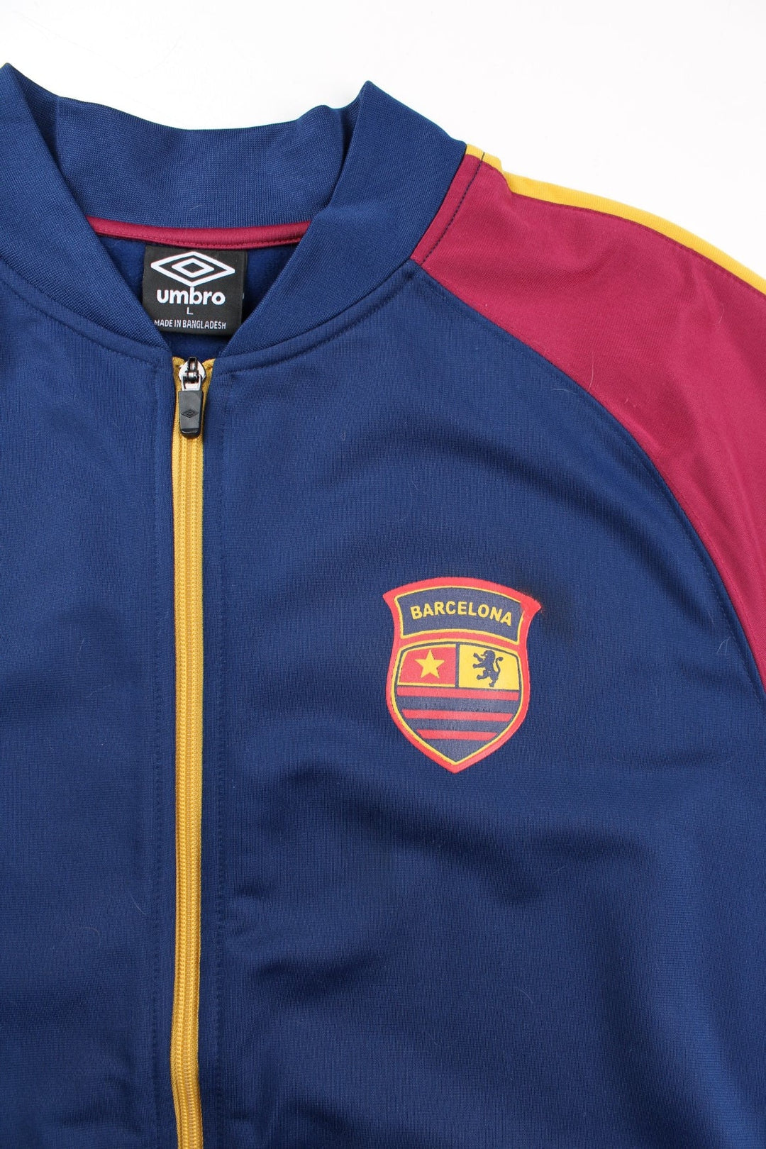 Umbro Barcelona Track Top in a blue colourway with red panelling and yellow stripe. Full zip with small club and brand logos on the front..