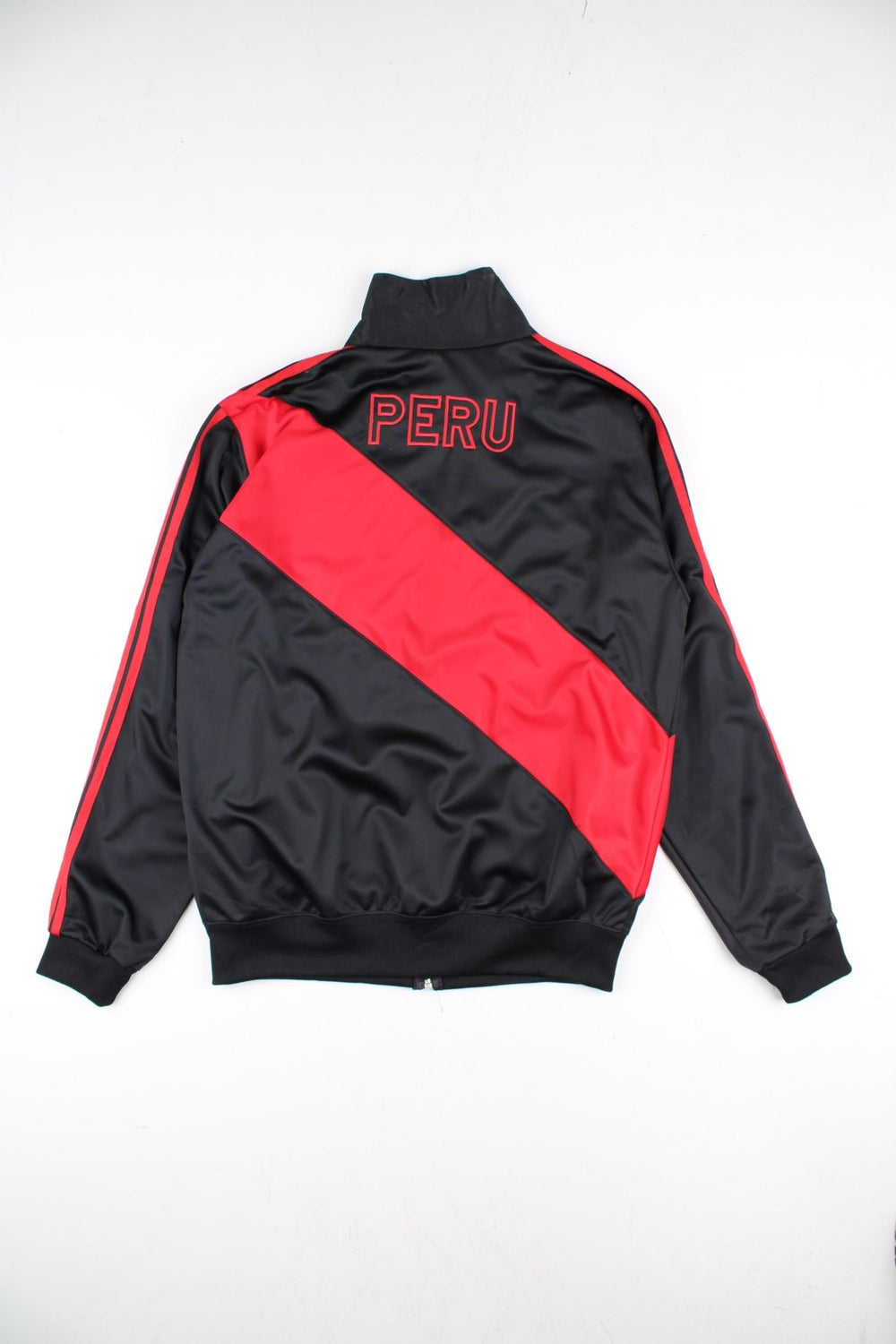 Adidas Rare Peru Track Top in a black colourway with classic red 3 stripe and red panelling. Small adidas logo and Peru badge on the front, with Peru lettering on the back. Full zip and double pockets.