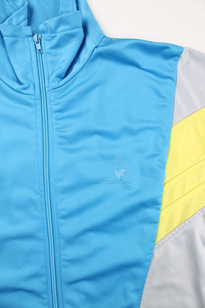 Le Coq Sportif Track Top in a grey colourway with blue and yellow panelling.Full zip with two side pockets. Buttons up and has side pockets.